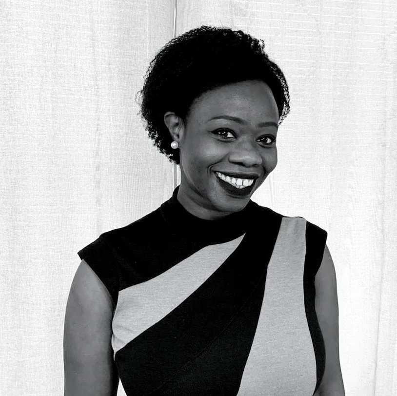 A black and white photography of N'Mah. She is looking into the camera and smiling. She is wearing a striped blouse.