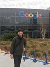 Inho stands in front of a building with the Google logo. In between are multicolored bike racks, some shrubs and a tree.