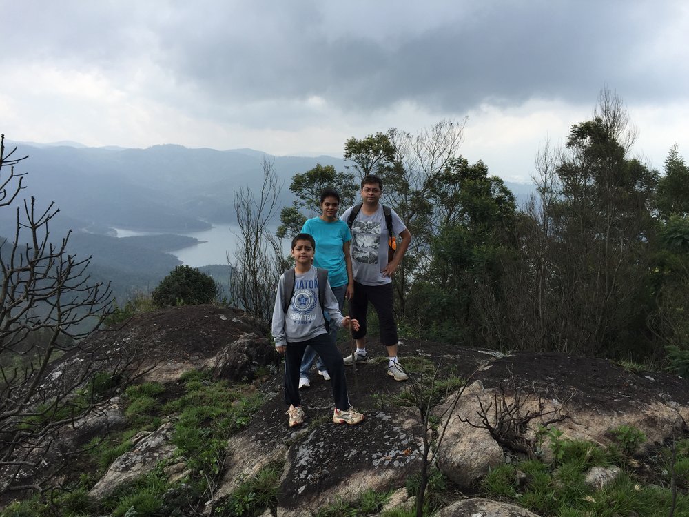 Manav stands on top of a mountain while on a hike with his wife and son.