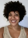 A photo of a woman with short black hair, wearing a tan tank top and hoop earrings, smiling against a white background