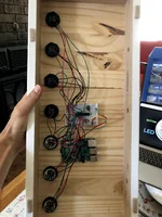 A hand is holding up a rectangular wooden box, featuring dark-colored buttons and multicolored wires.