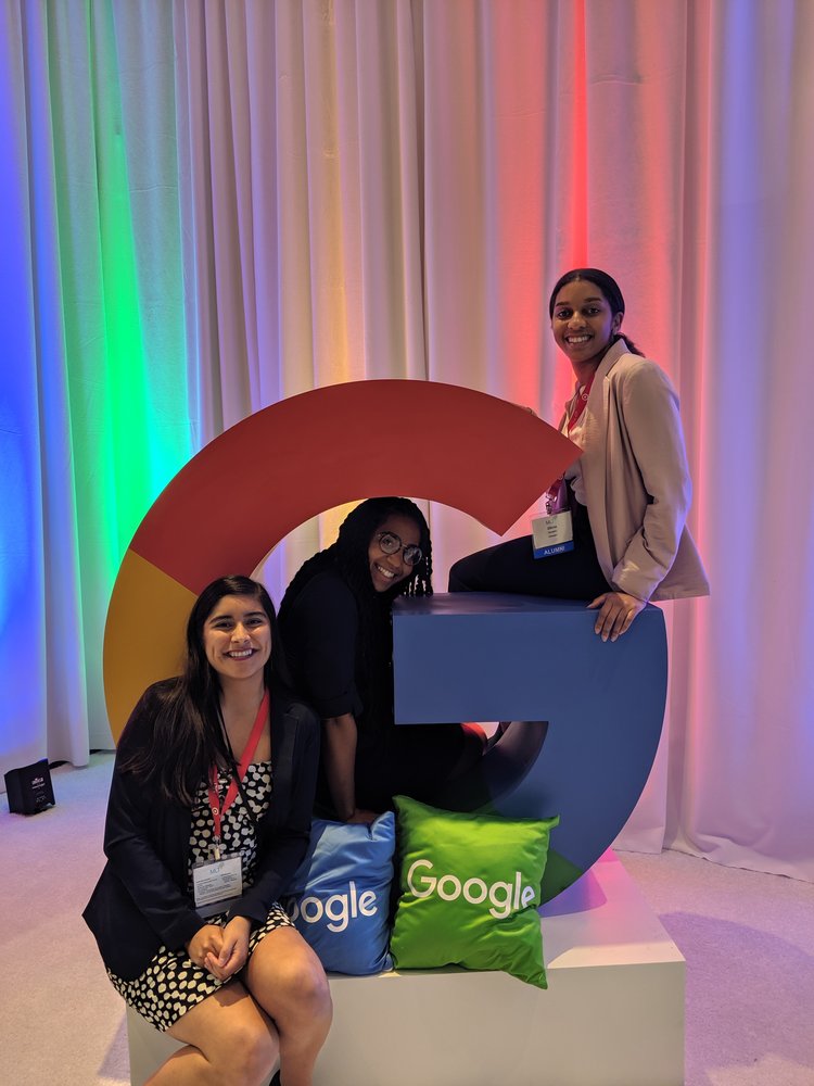 Three people sitting around a large “G” sculpture.