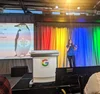 Avital speaking next to a podium with a Google logo and a slide with a penguin on it.