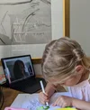 photo of a girl coloring while having a virtual video call with her grandma on a laptop