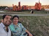 A photo of a couple sitting on a lawn in front of a park during sunset.