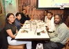 A group of people smile for a photograph taken at a restaurant while food is on the table.