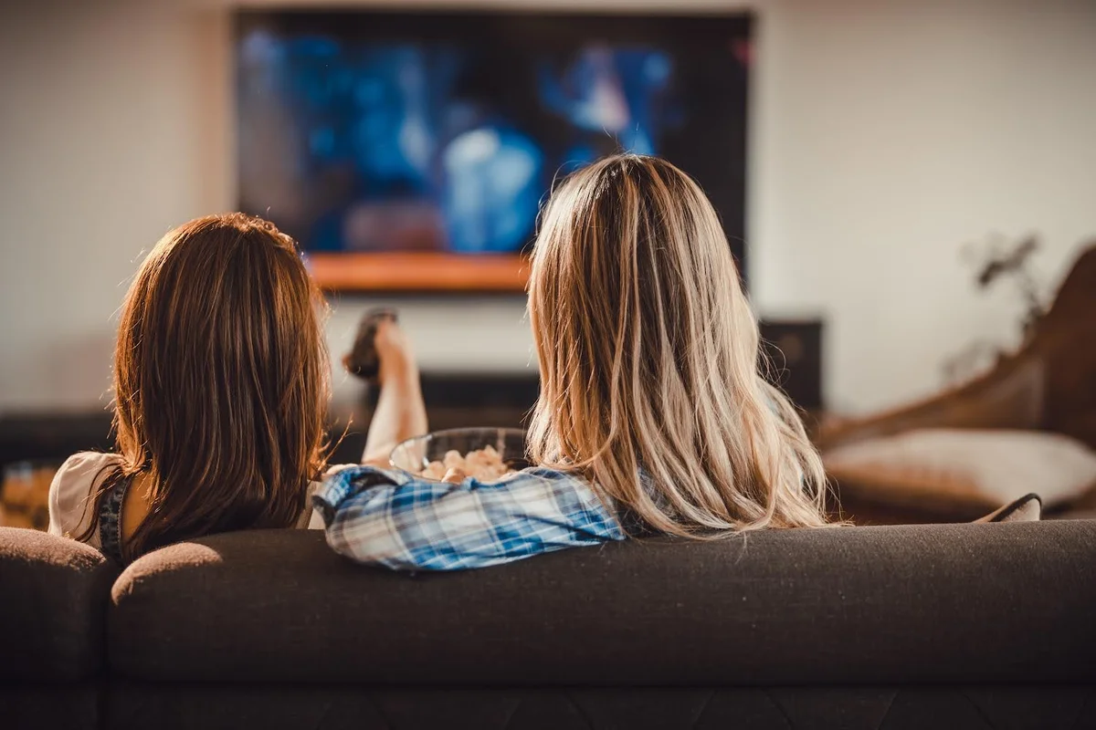 Two women sitting on a couch watching TV