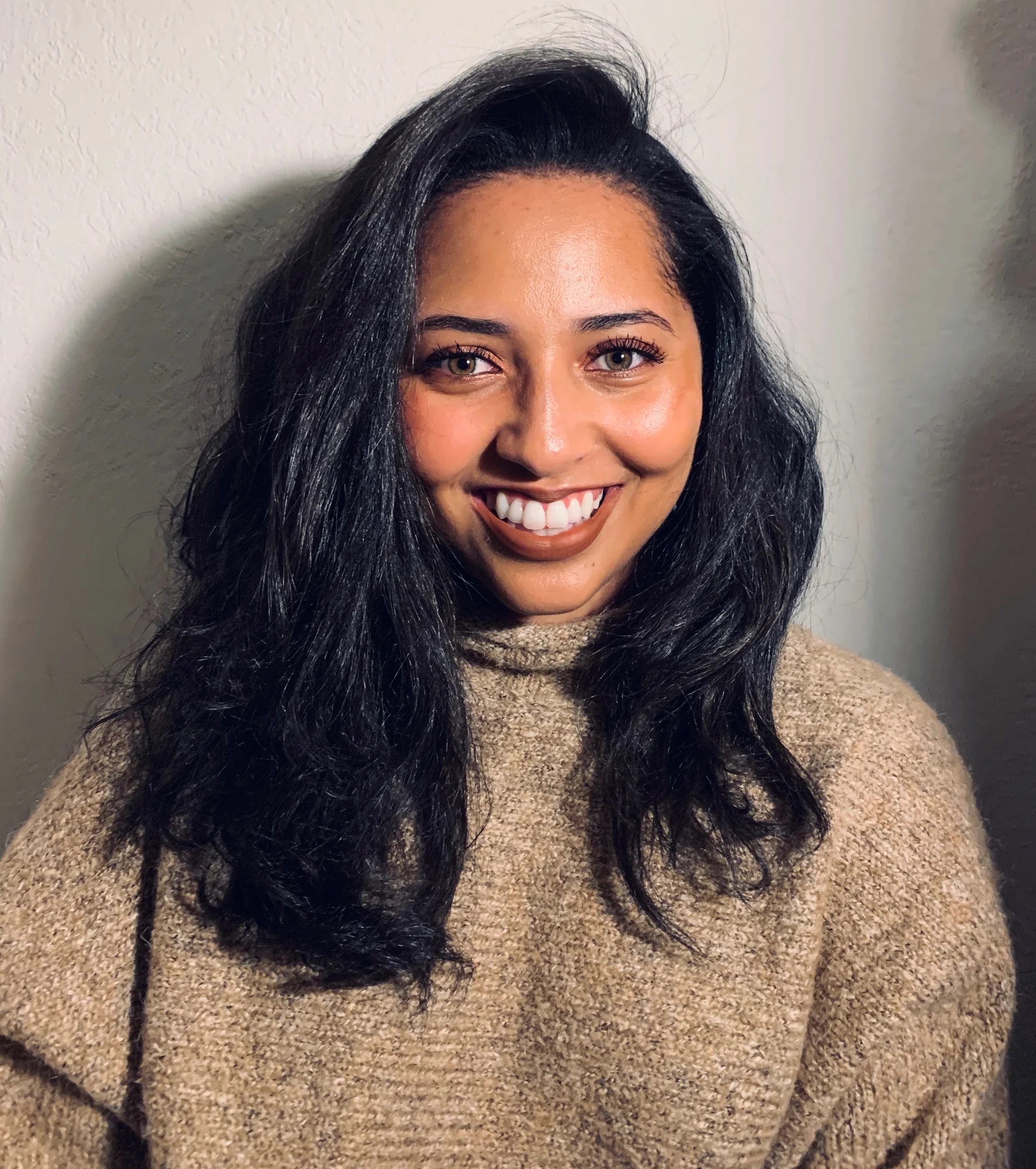 A photograph of Cherish looking into the camera and smiling. She is swearing a khaki colored sweater.