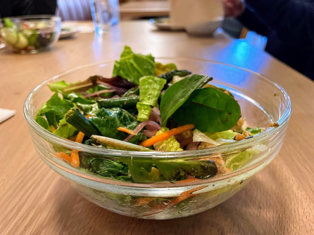 A photo of a salad in a clear glass bowl sitting on a desk.