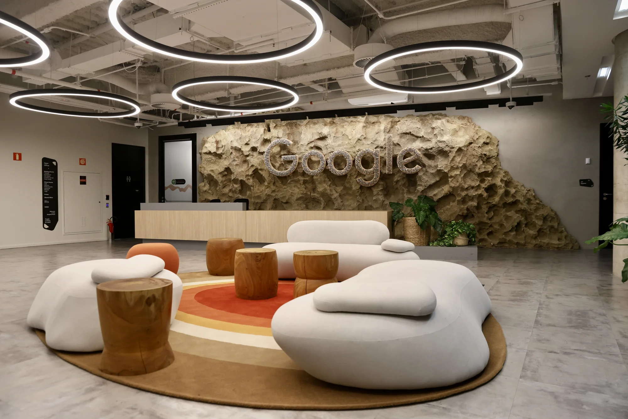 recepção do novo escritório com sofás, bancos, luminárias circulares e um painel escrito Google