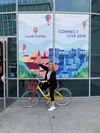 A woman sitting on a bicycle in front of a sign that says “Local Guides Connect Live 2019”