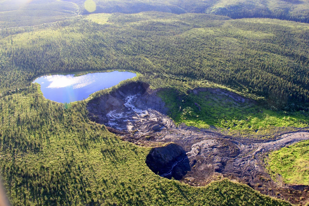 Aerial photo of an arctic landscape with a lake and a permafrost slump — a brown landslide caused by the thawing of ground ice.