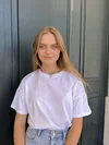 A woman with long blonde hair and wearing a white t-shirt and jeans looks at the camera.