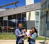 Dennis and his wife, Tiffany, standing and smiling in front of a Google building, while holding their twins, Gabriella and Mason