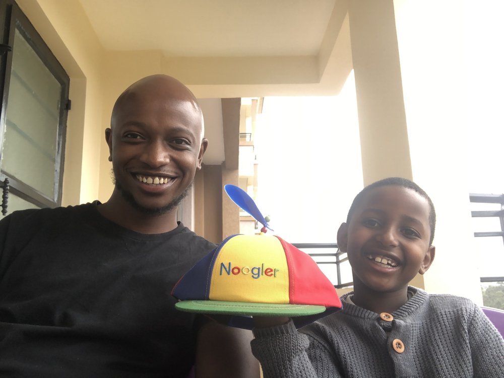 Andrew and his son smile at the camera holding a Noogler hat.