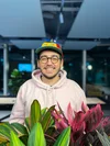 Rand wears a multi-colored “Noogler” propeller hat and stands behind a plant.