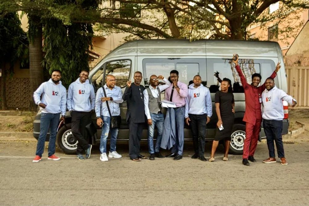 The Ripples Nigeria team stand in front of a minivan smiling to the camera in corporate jumpers and work attire.