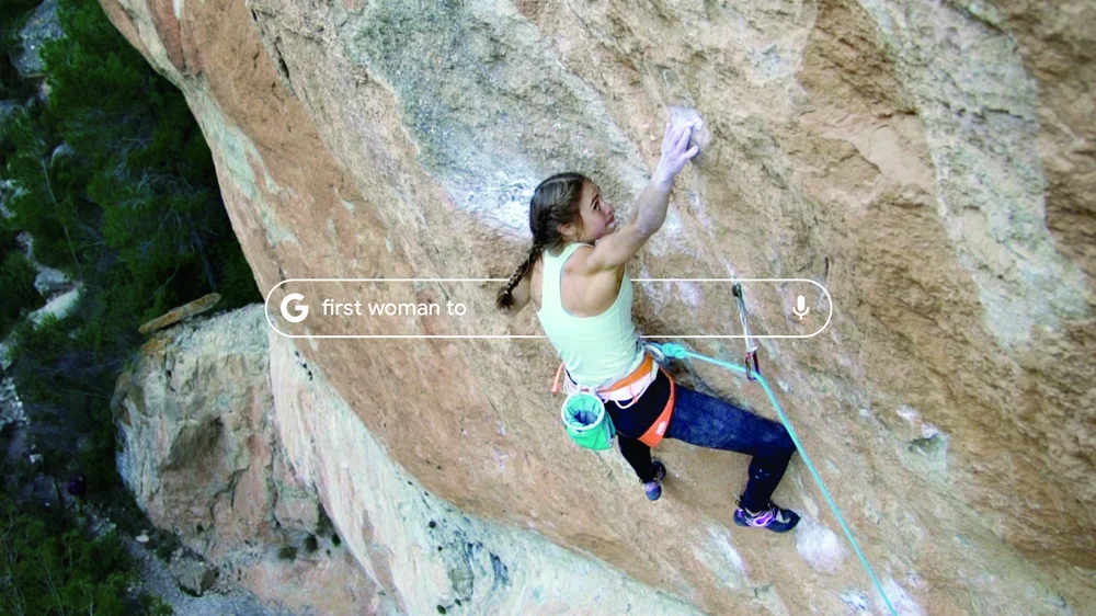 An image of a woman climbing a mountain with a Google search bar noting "first woman to"