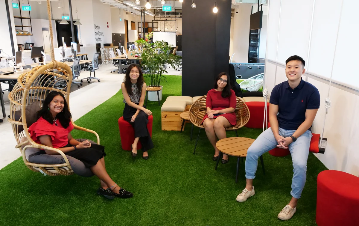 An image of Skills Ignition trainee Gaviota with three of her fellow trainers, two women, one man, in the offices of Omnicom Media Group — their host company. They’re sitting on seats in a casual area with astroturf on the floor.