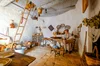 White walled interior with light brown wooden paneling and small crafted furniture and baskets, with a woman in the corner.