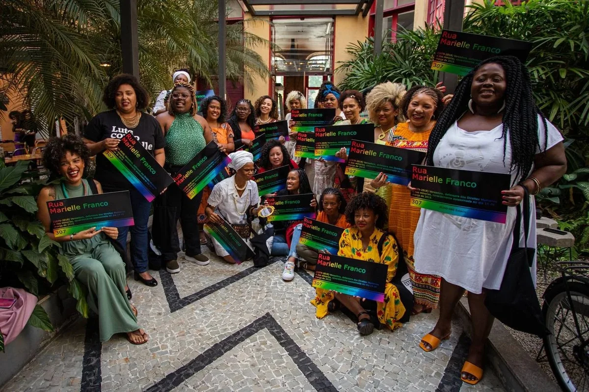 Mulheres negras posam para foto com placa da Rua Marielle Franco.