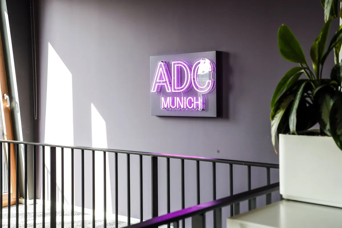 An einer Wand hängt ein Neon-Zeichen, das ADC Munich zeigt