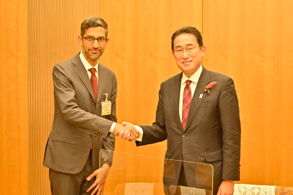 Two people looking at the camera, in suits, shaking heads.