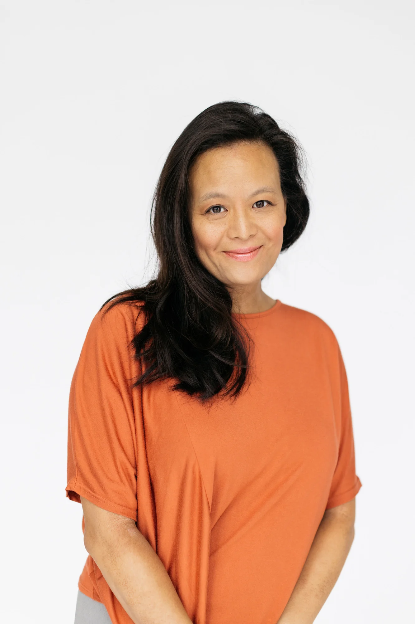 Photograph of Jessica Yu smiling directly at camera wearing a bright orange shirt. Jessica has tan skin and long black, straight hair.