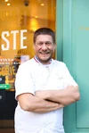 A photograph of baker Joel Defives, smiling, arms folded, outside his bakery