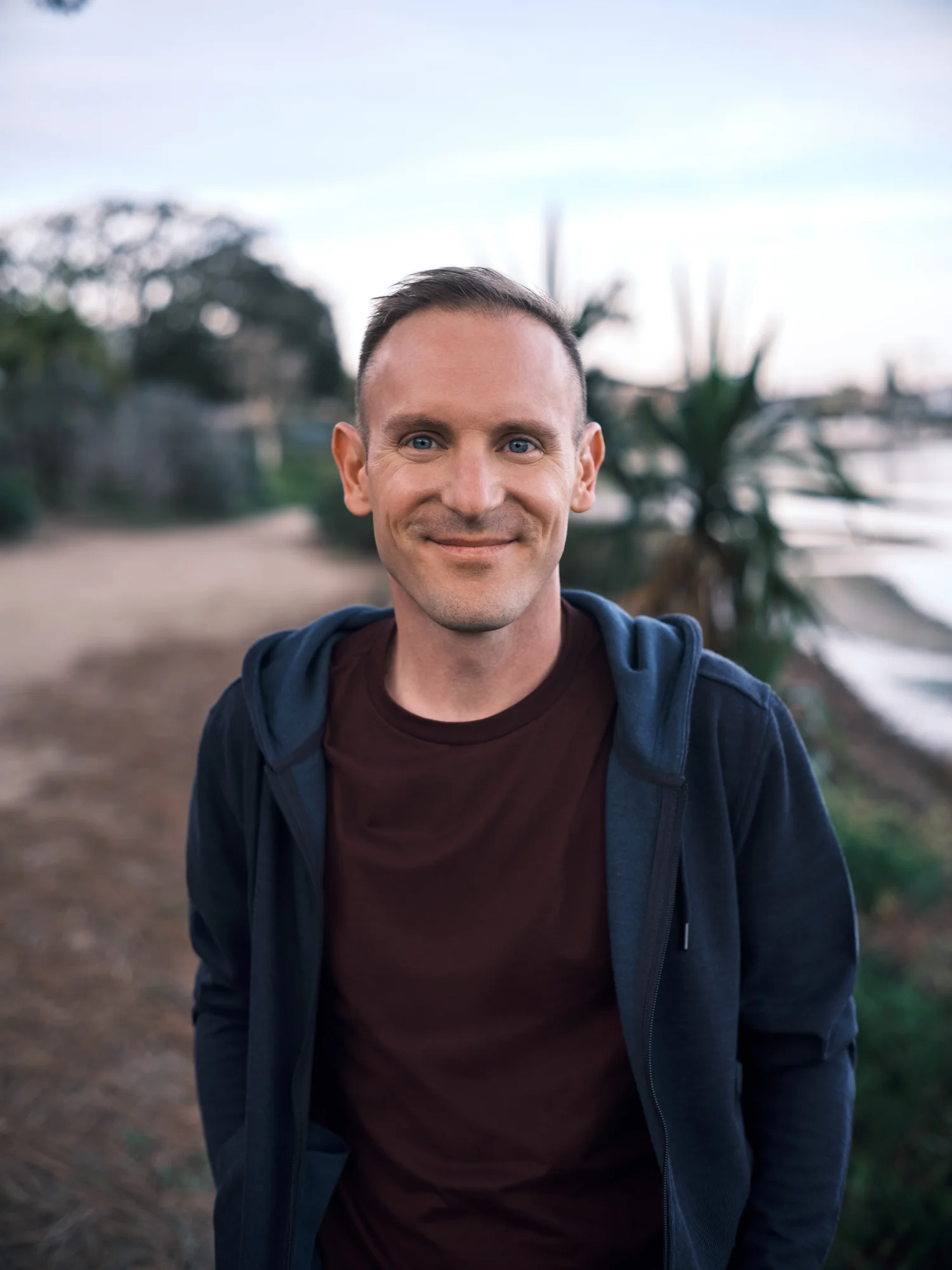 Headshot of John standing on a hiking path near a lake with greenery behind him.