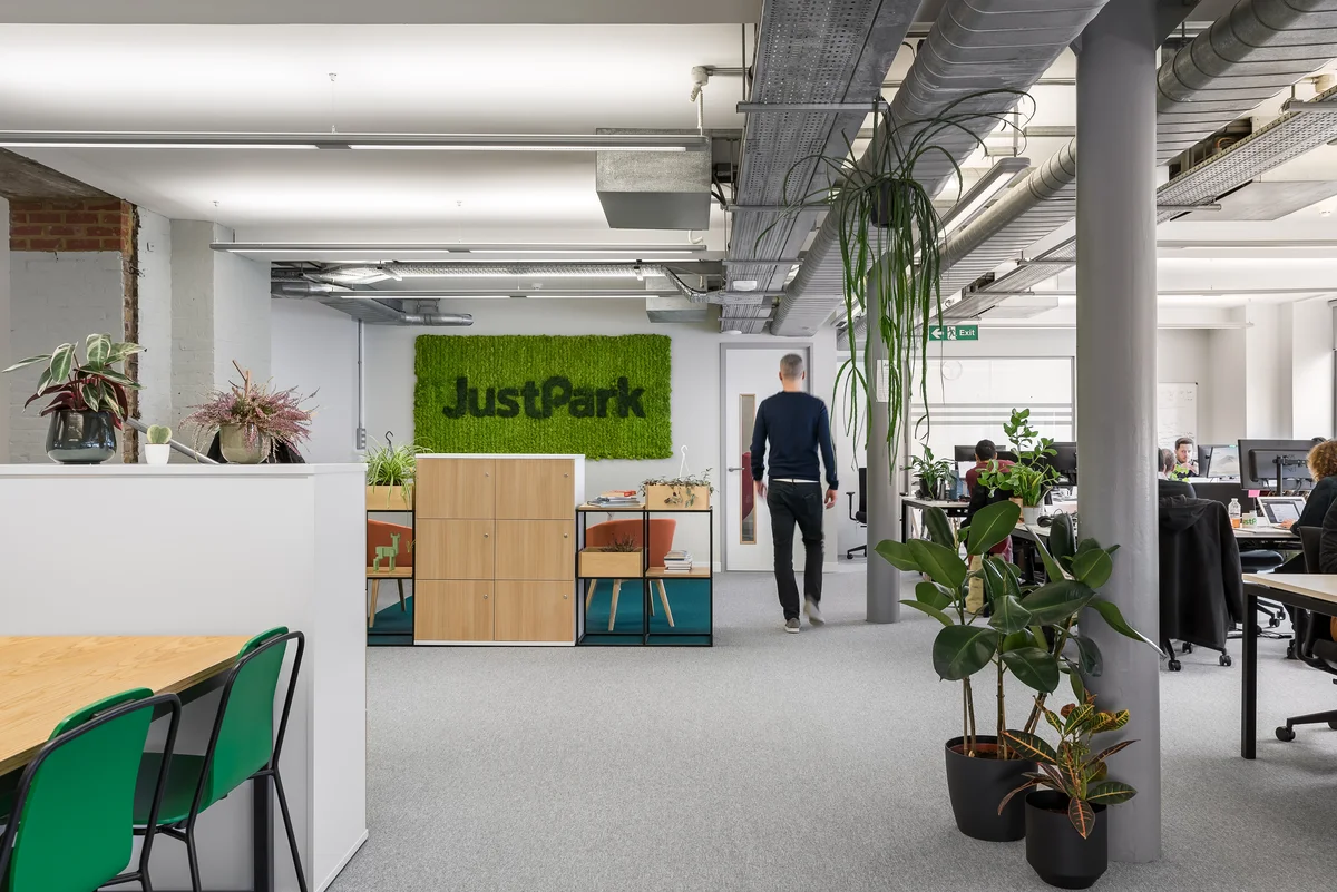 Man walking in an open plan office with a large sign saying JustPark