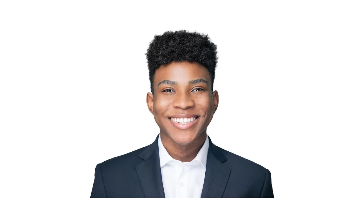 Kahlil Greene smiles, wearing a navy blue blazer and white dress shirt. He wears his brown hair in a flat top style.