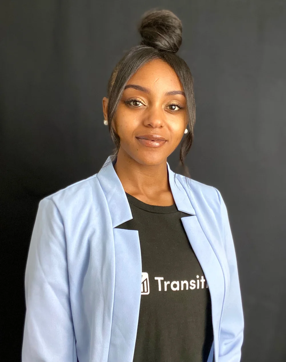 Kayla Wright-Jackson looks into the camera wearing a powder blue blazer over a black Transition t shirt. She wears golden hoops and has her hair up in a bun.