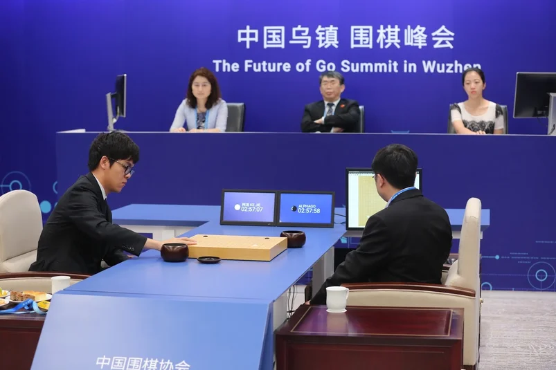 Two people sit at a table in front of a judging panel