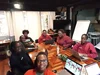 A group of seven people sitting around a table, smiling and working on laptops.