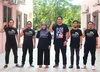 A group of people standing and smiling at the camera with one first in the air, wearing t shirts that say “kitajaga.co”