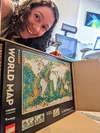 A woman with brown curly hair smiling into the camera and holding a world map LEGO box.