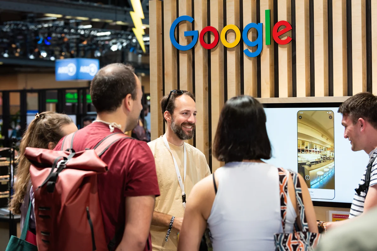 Gäste am Google-Stand mit Google-Logo und Monitor im Hintergrund