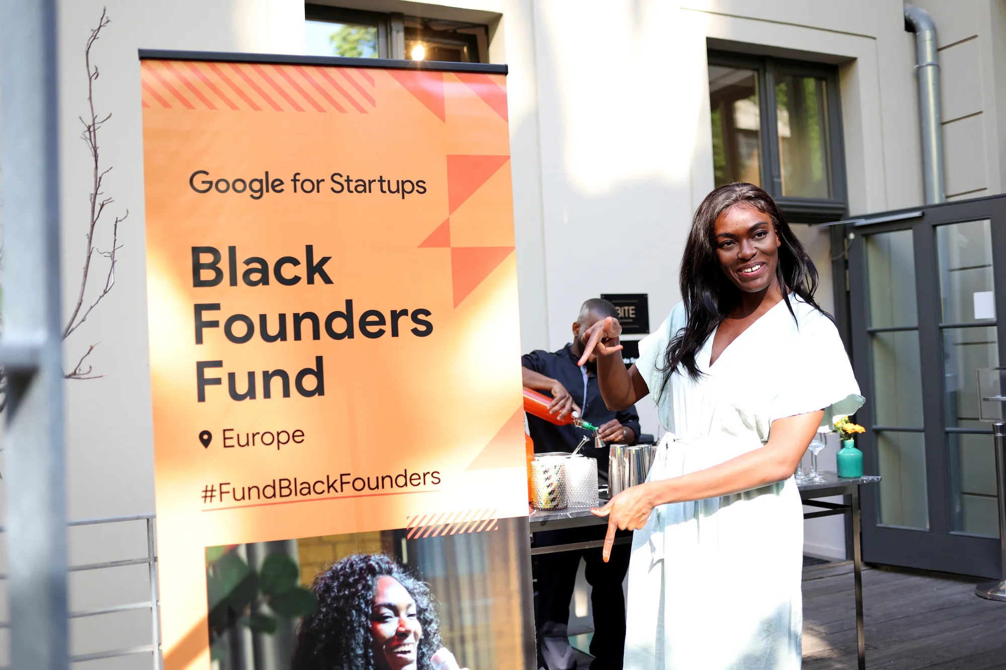 Gründerin Deborah Choi posiert vor einem Roll-up-Plakat, auf dem „Black Founders Fund Europe“ steht und ein Foto von ihr zu sehen ist.