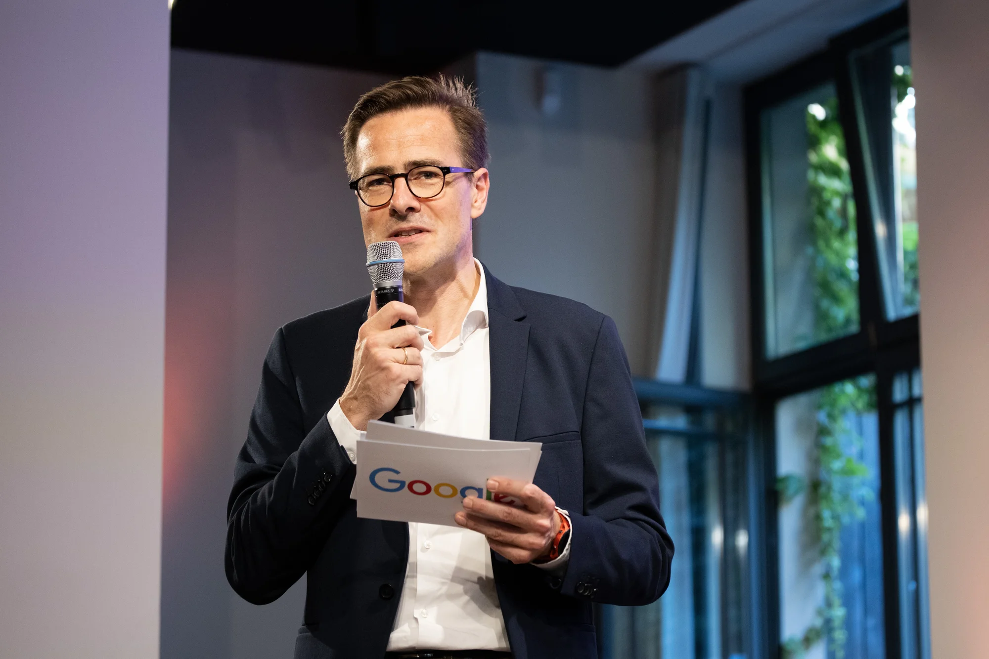 Philipp Justus steht auf der Bühne beim Black Founders-Event. In seiner rechten Hand hält er ein Mikrofon, in seiner linken Hand Moderationskarten mit dem Google-Logo.