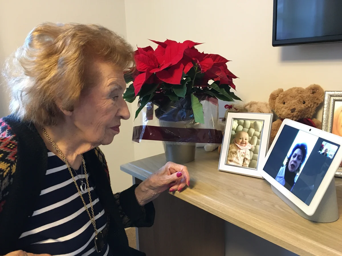 Image shows an elderly woman using a Nest Hub Max that's sitting on her desk to have a video call with her daughter.