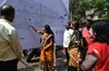 A woman in a sari pointing at a location on a map, with a group of people behind her looking at the map.