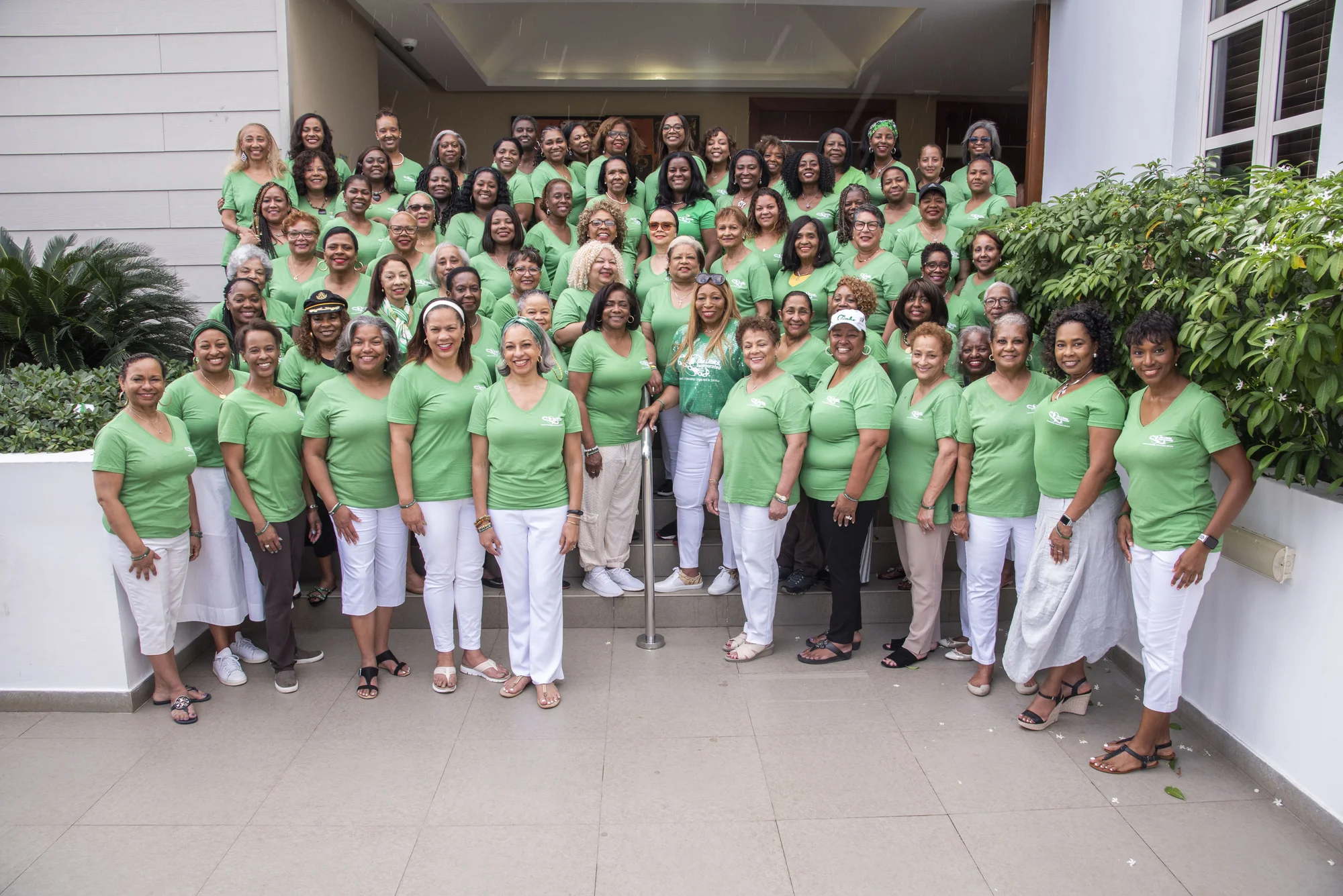 A group of dozens of women wearing light green shirts standing on steps outdoors.