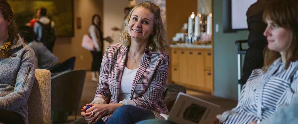 Article's hero Agnieszka sits between two other women in a conversation circle. In the background is a coffee bar and other people standing in the room.media