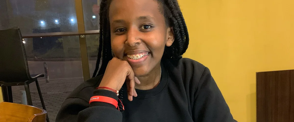 Angela, wearing a black crew neck sweater and red bracelets, smiles at the camera.