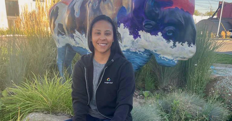 A woman in a black Google Cloud sweater sits on a rock in front of a painted sculpture of a buffalo.