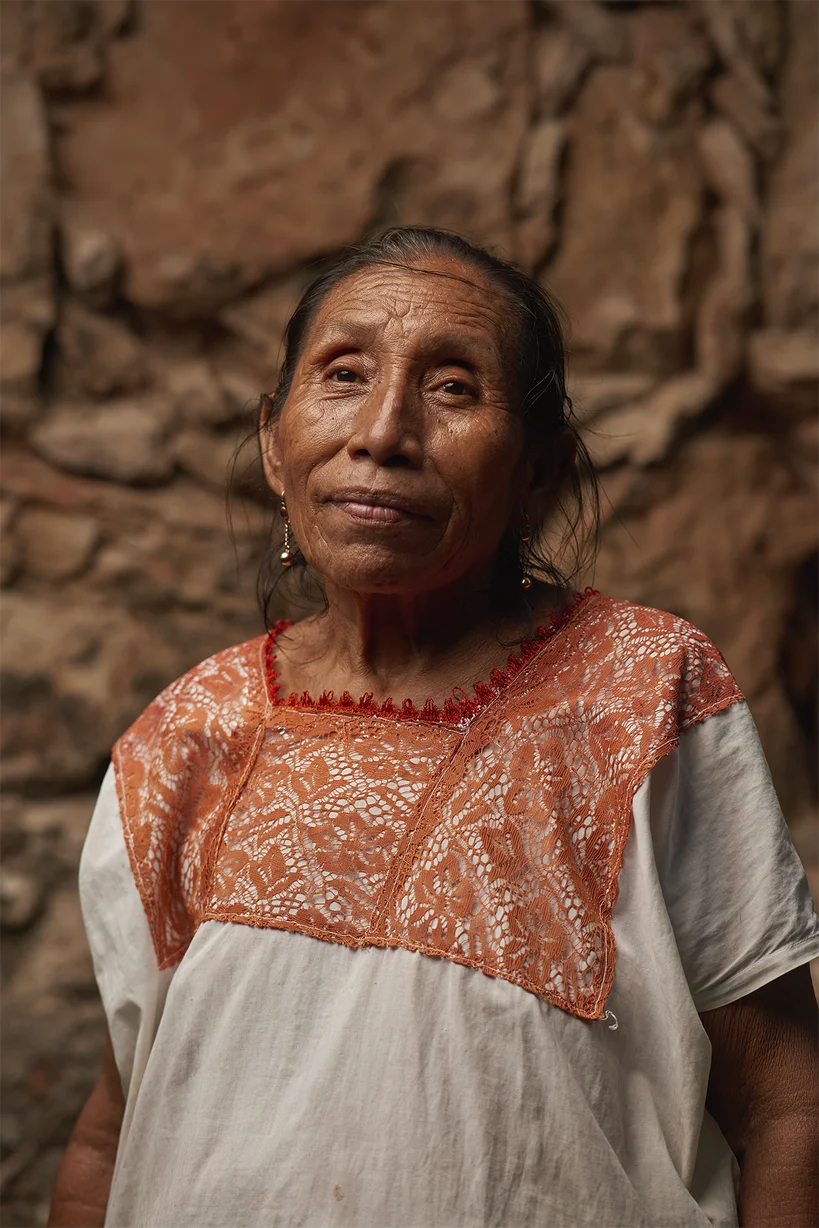 A Maya language speaker smiles at the camera against a red, rocky background.