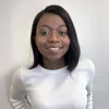 A Black woman with shoulder-length brown hair and wearing a white shirt smiles at the camera.