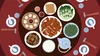 a birds eye view of a round table with several bowls, chopsticks, and dishes like rice, greens, and dumplings