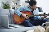 Man playing guitar on gray sofa